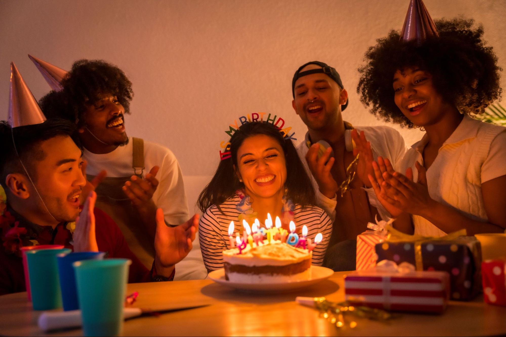 People surrounding a cake with candles and gifts. 