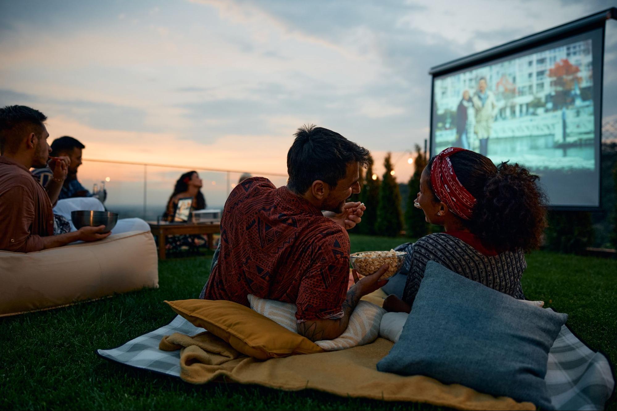 A few couples are enjoying a movie and watching outdoors.