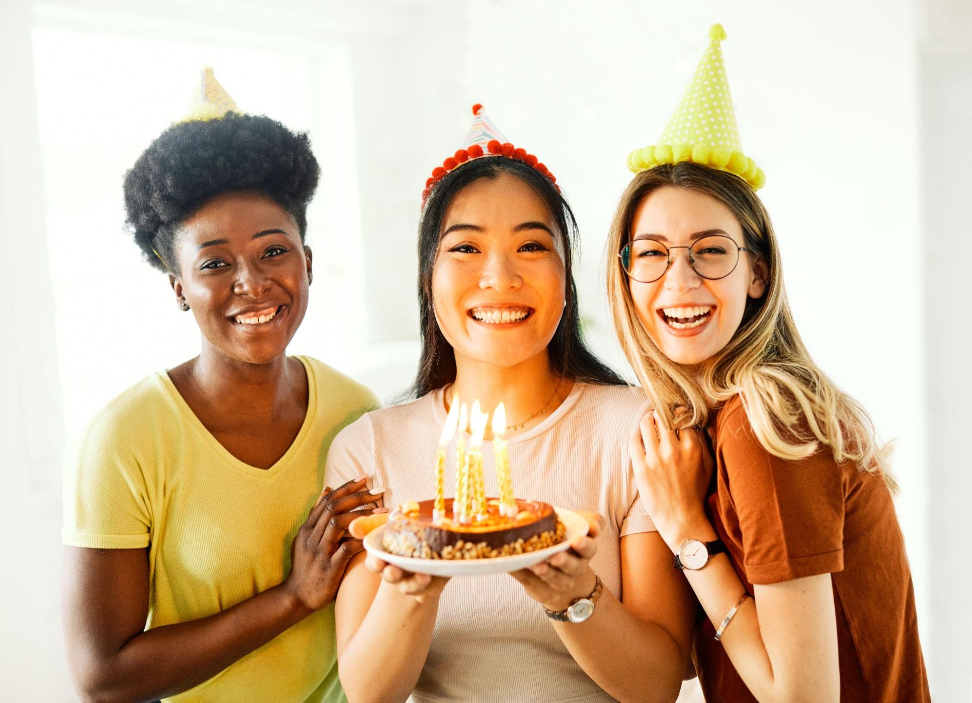 Three women with birthday hats and a cake. 