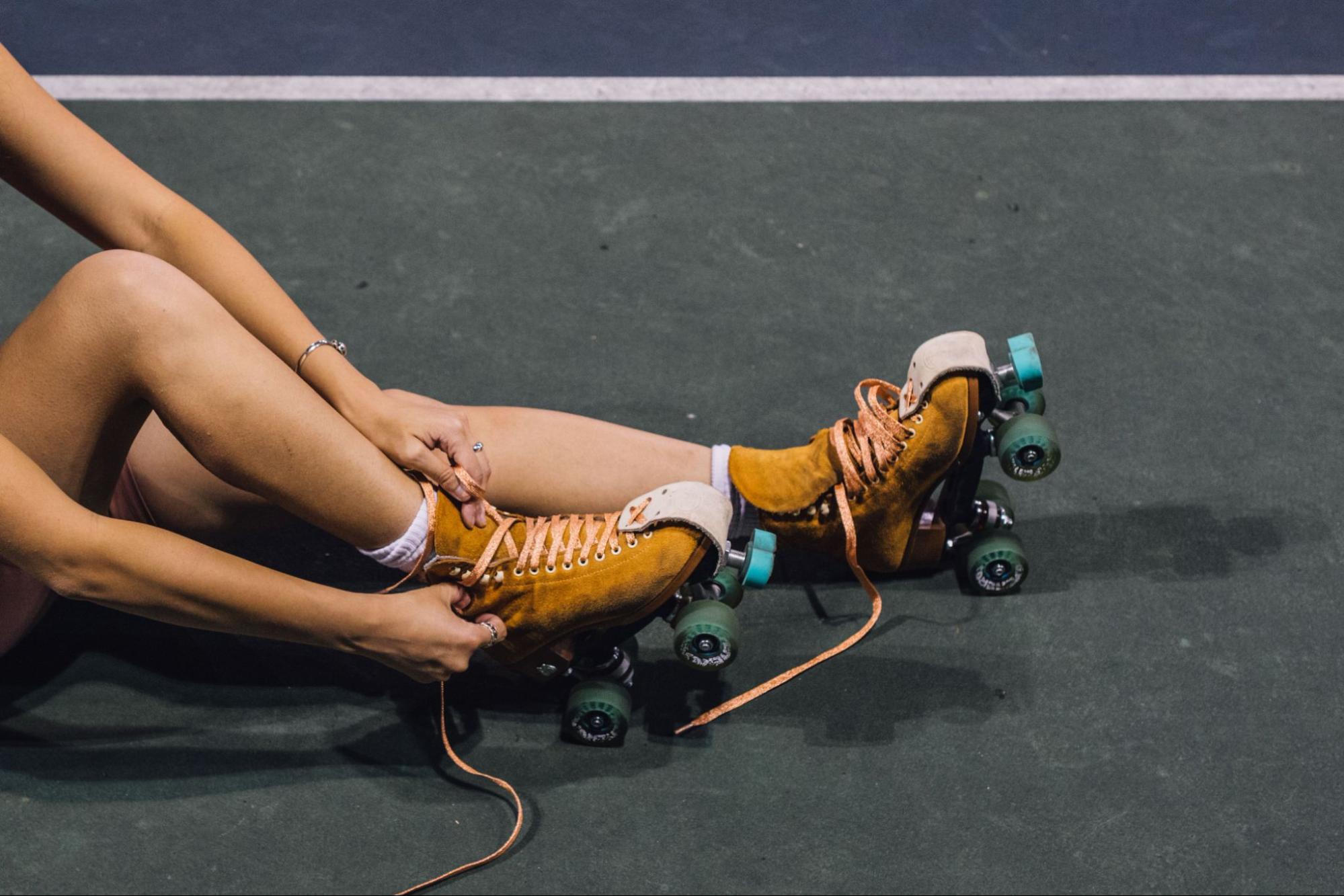 A woman lacing up her rollerblades at a roller rink.