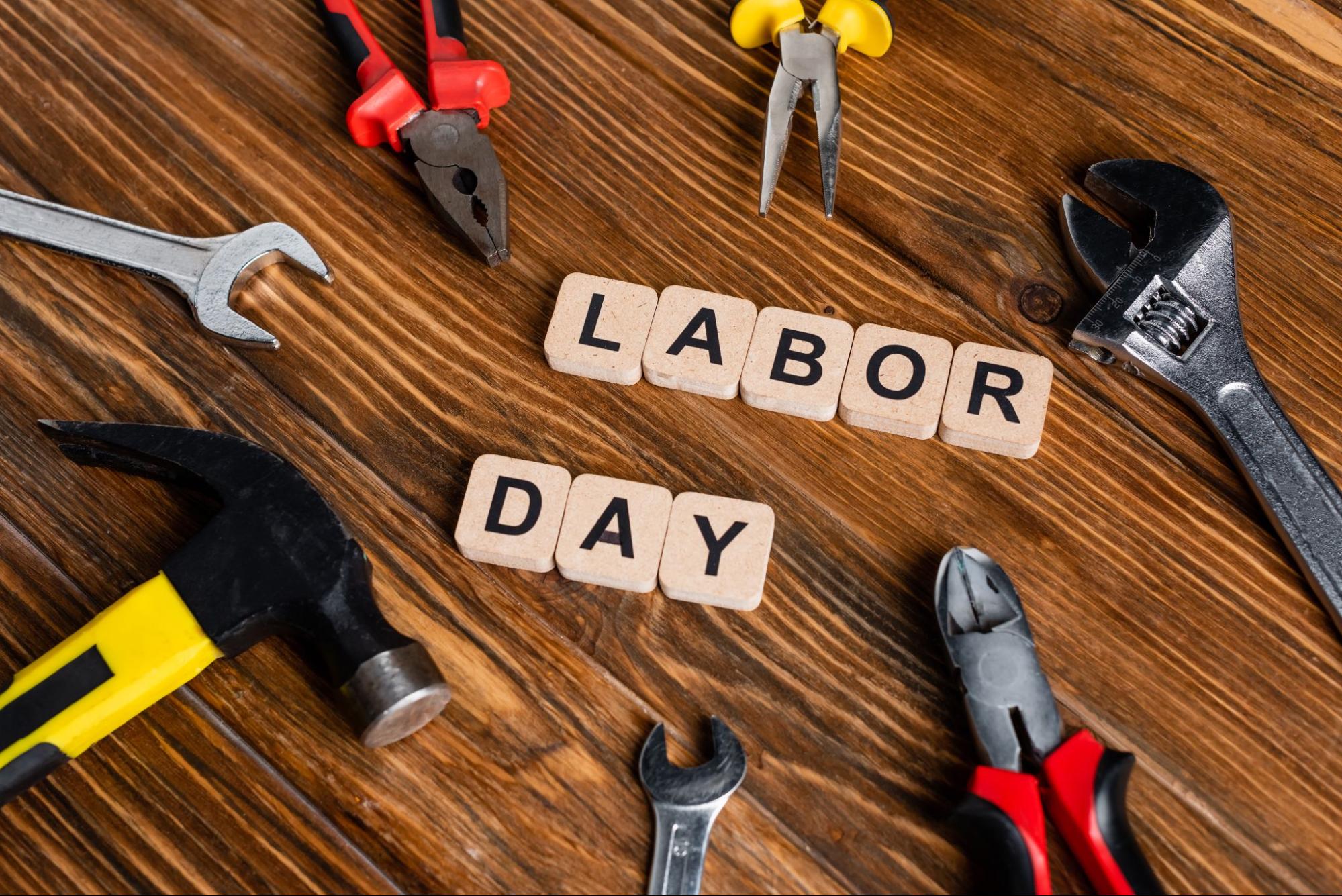 “Labor day” on wooden blocks next to various tools on a wooden surface. 