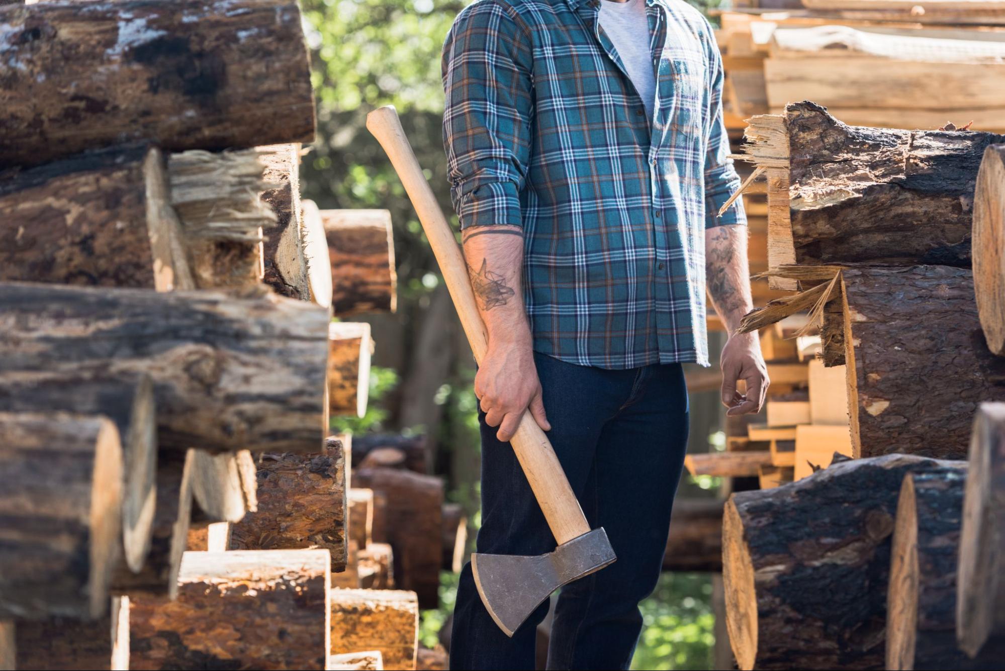 Man with an axe next to cut logs of wood. 