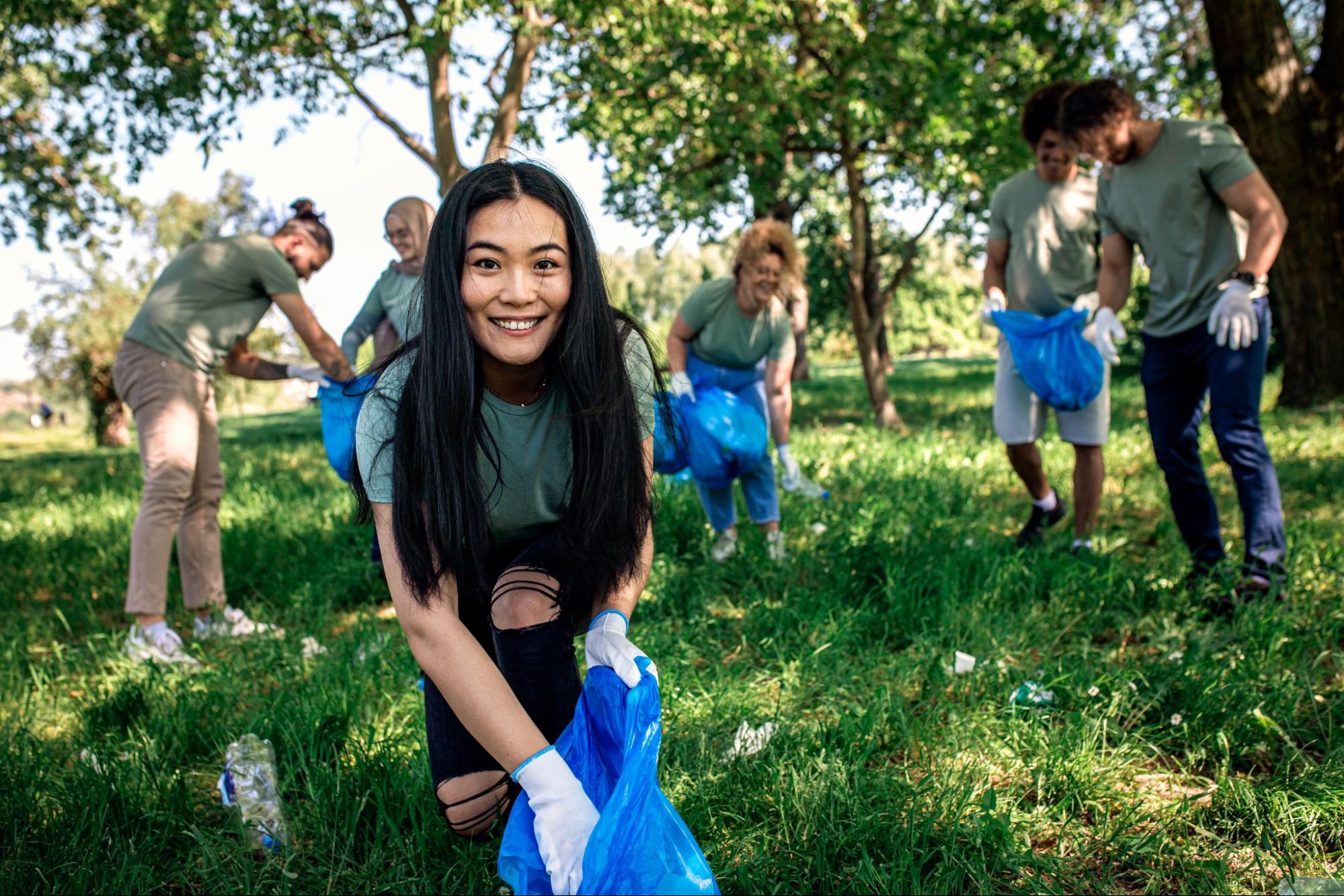 Woman smiling and picking up trash next to men and women in the background holding trash bags. 