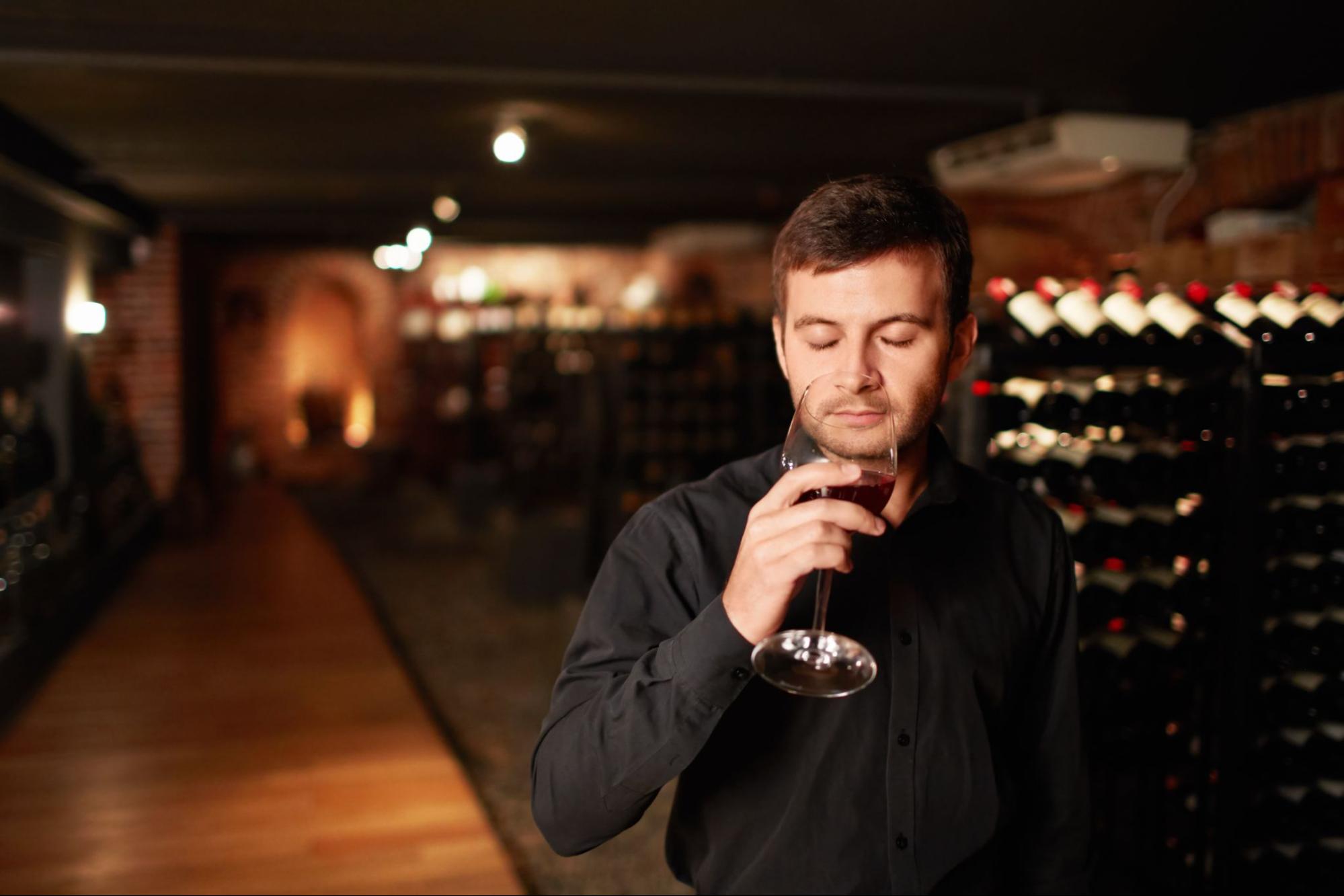 A man wearing a black dress shirt is tasting wine at a winery.