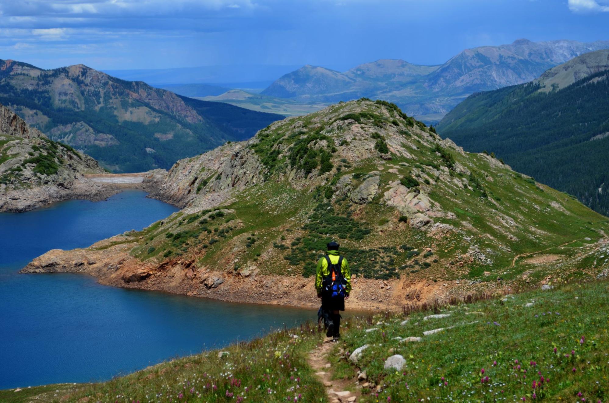 A man on a hiking trail with mountains and a lake in Colorado. 