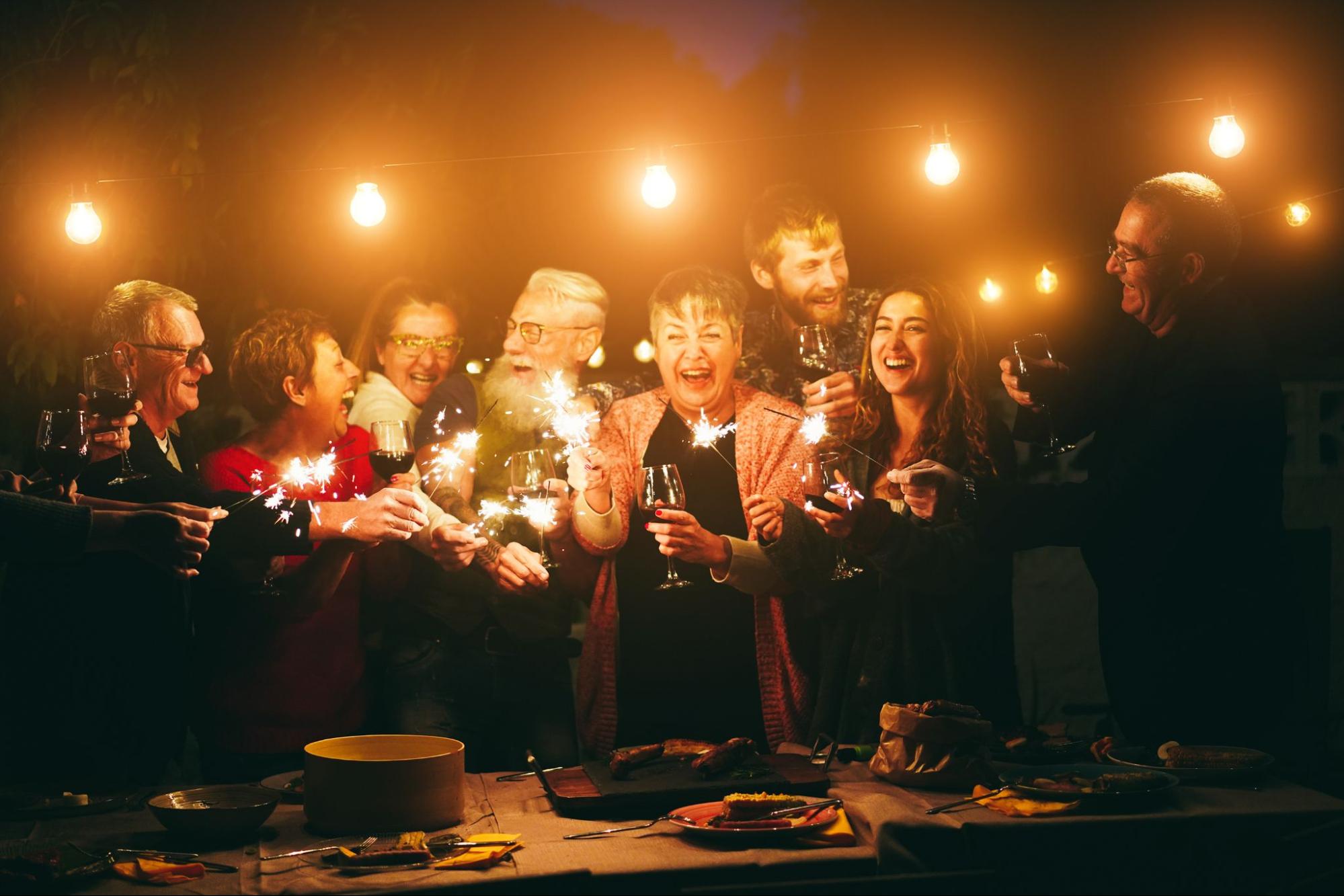 People with sparklers smiling and holding drinks next to overhanging lights. 