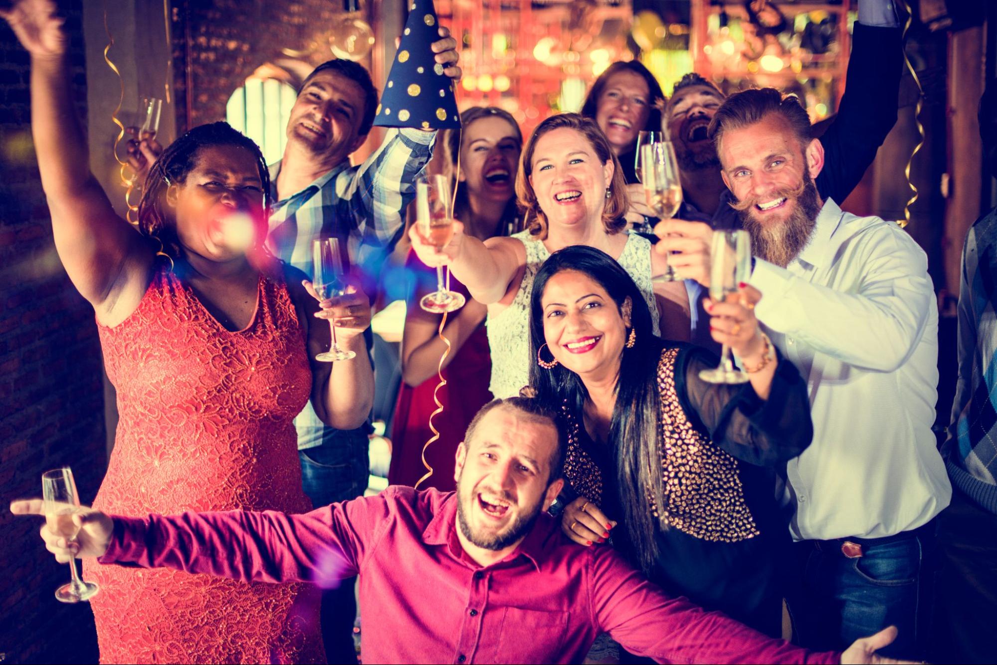 Friends posing for a picture, holding wine glasses in a celebratory toast under sparkling tinsels at an elegant restaurant.