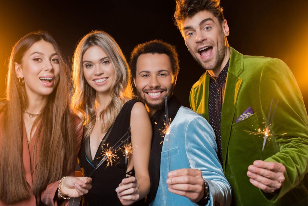 Two women and two men smiling and holding sparklers at a party. 