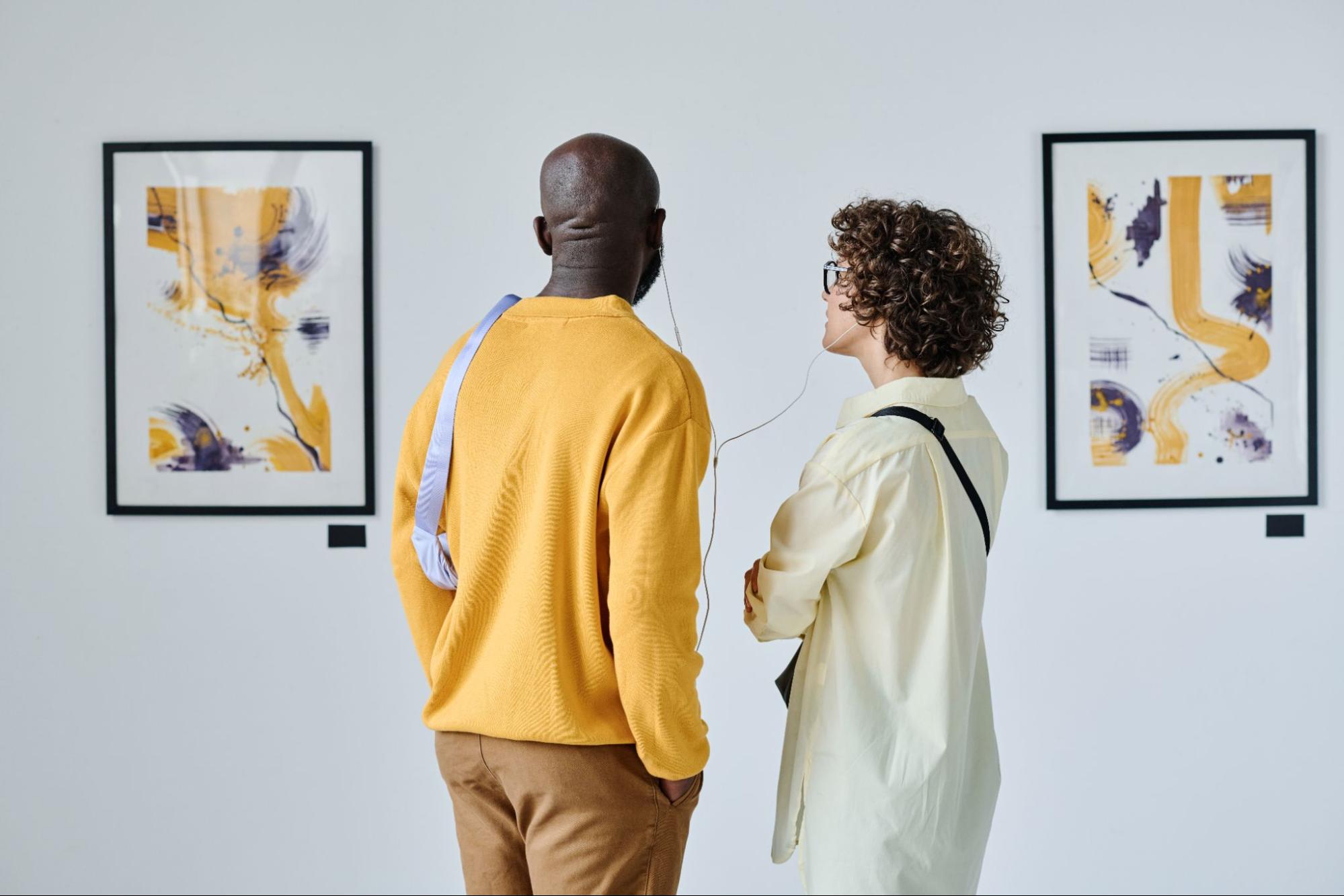 Man and a woman wearing headphones and looking at artwork.