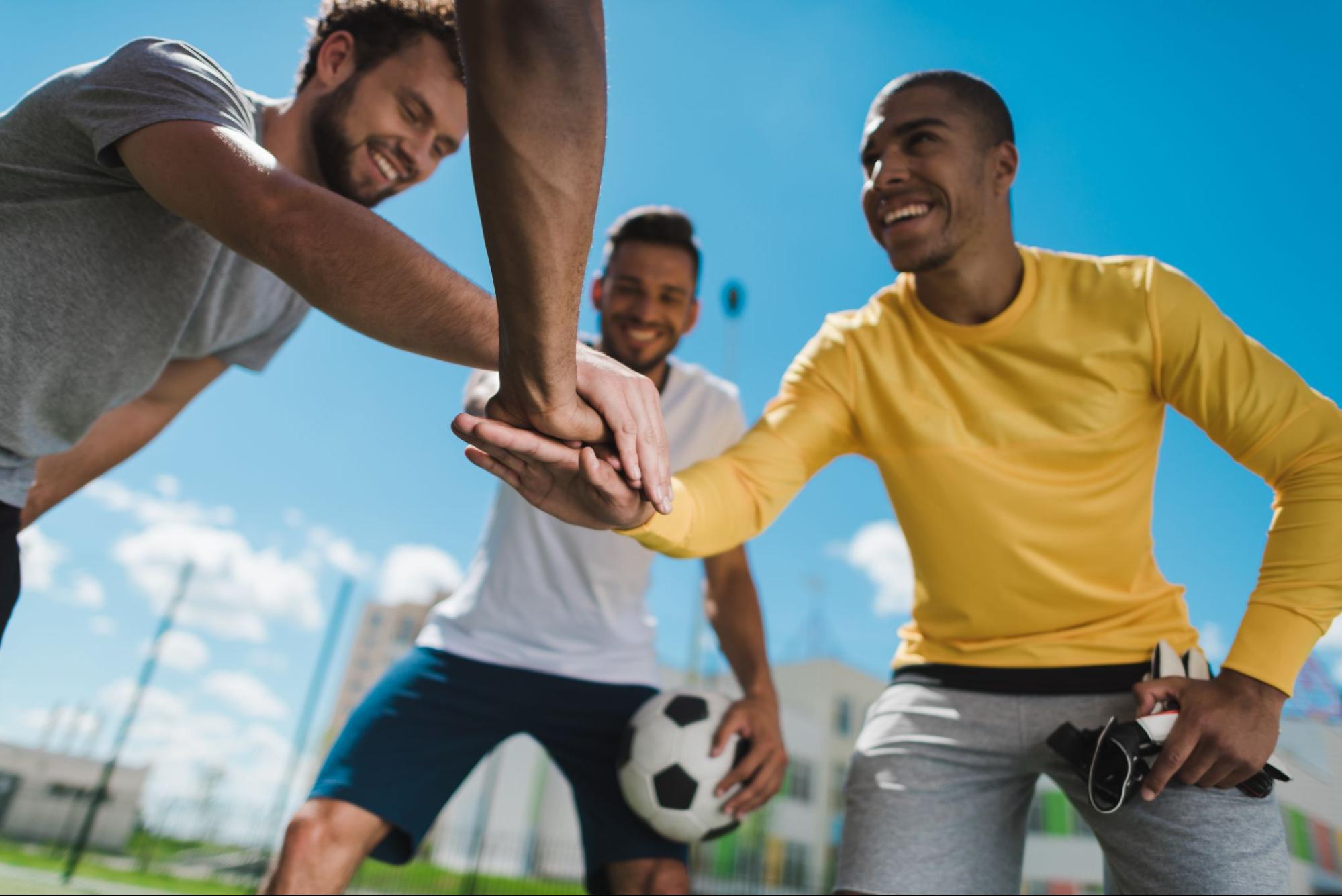 A low-angle view of cheerful multiethnic friends holding hands together before starting a soccer game.